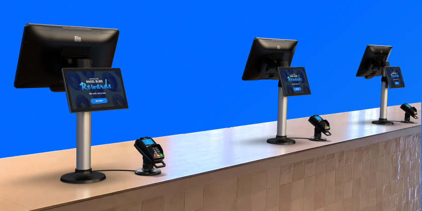 Mehrere Elo-Touchscreen-Displays, die auf Ständern entlang einer Ladentheke angebracht sind und jeweils digitale Werbeinhalte anzeigen, wobei davor Zahlungsterminals aufgestellt sind, um In-Store-Werbung und Interaktionen am Point of Sale zu unterstützen.